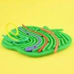 a green toy with colorful linesSilikoninė sensorinė užsiėmimų lentutė Obuolys 17cm